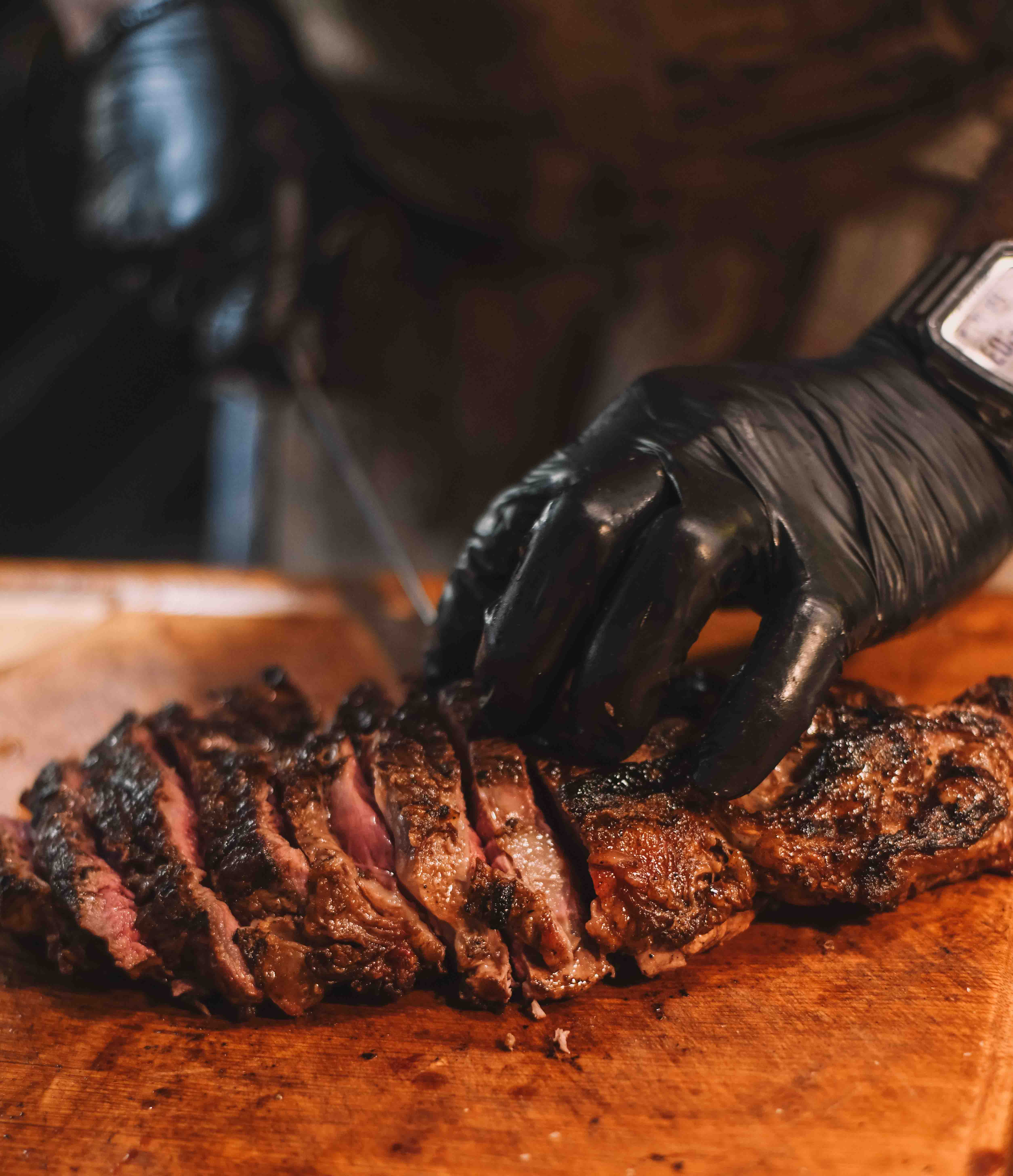 Carne grelhada sendo fatiada com luvas pretas